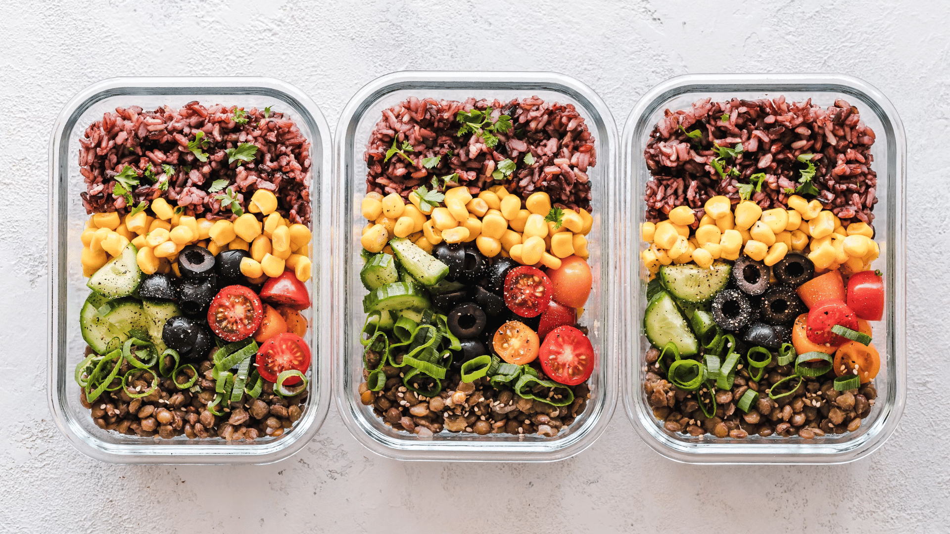 three glass meal prep containers filled with rice corn vegetables olives and lentils
