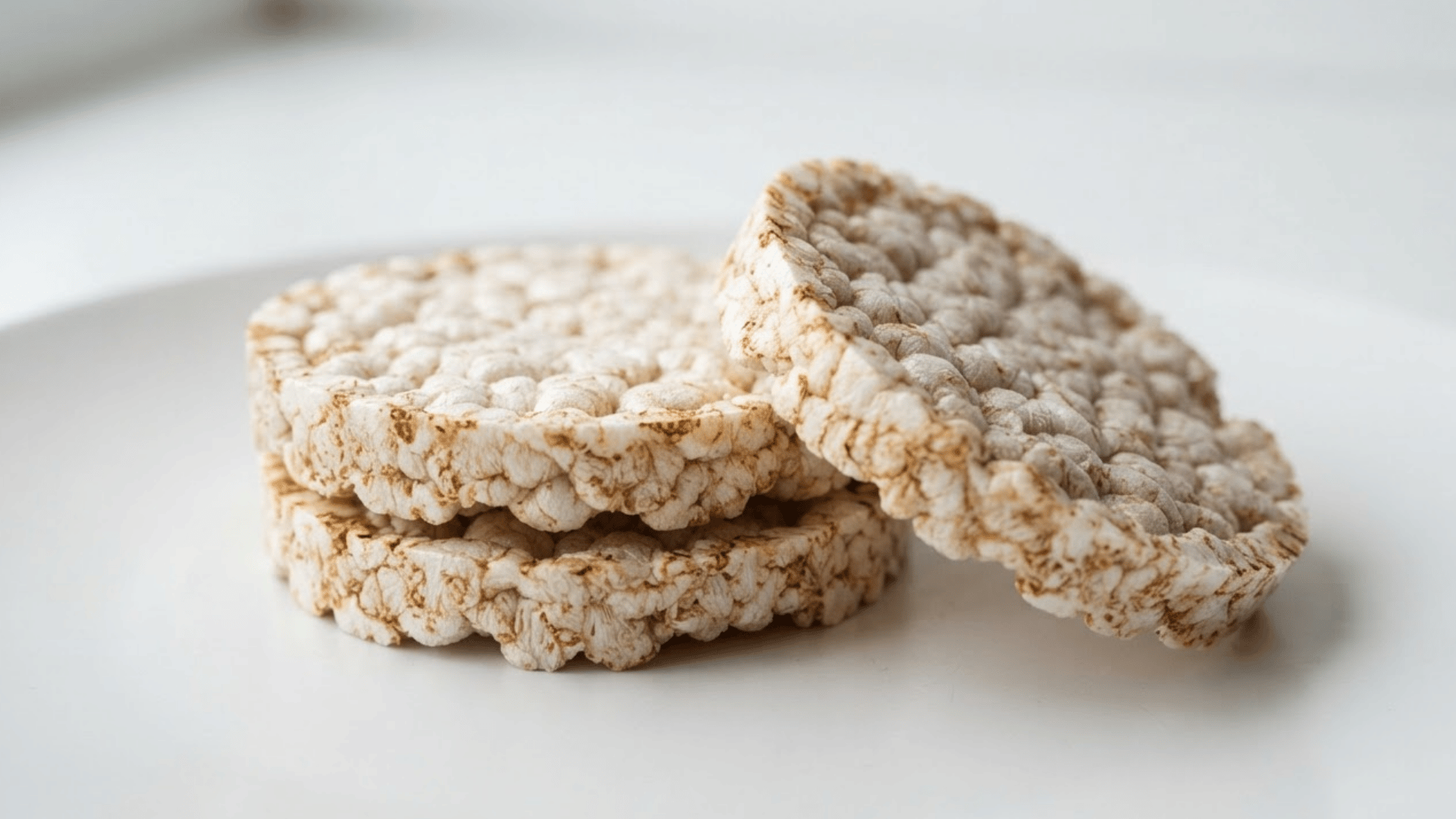 three plain puffed rice cakes stacked on a white plate showing their crisp airy texture