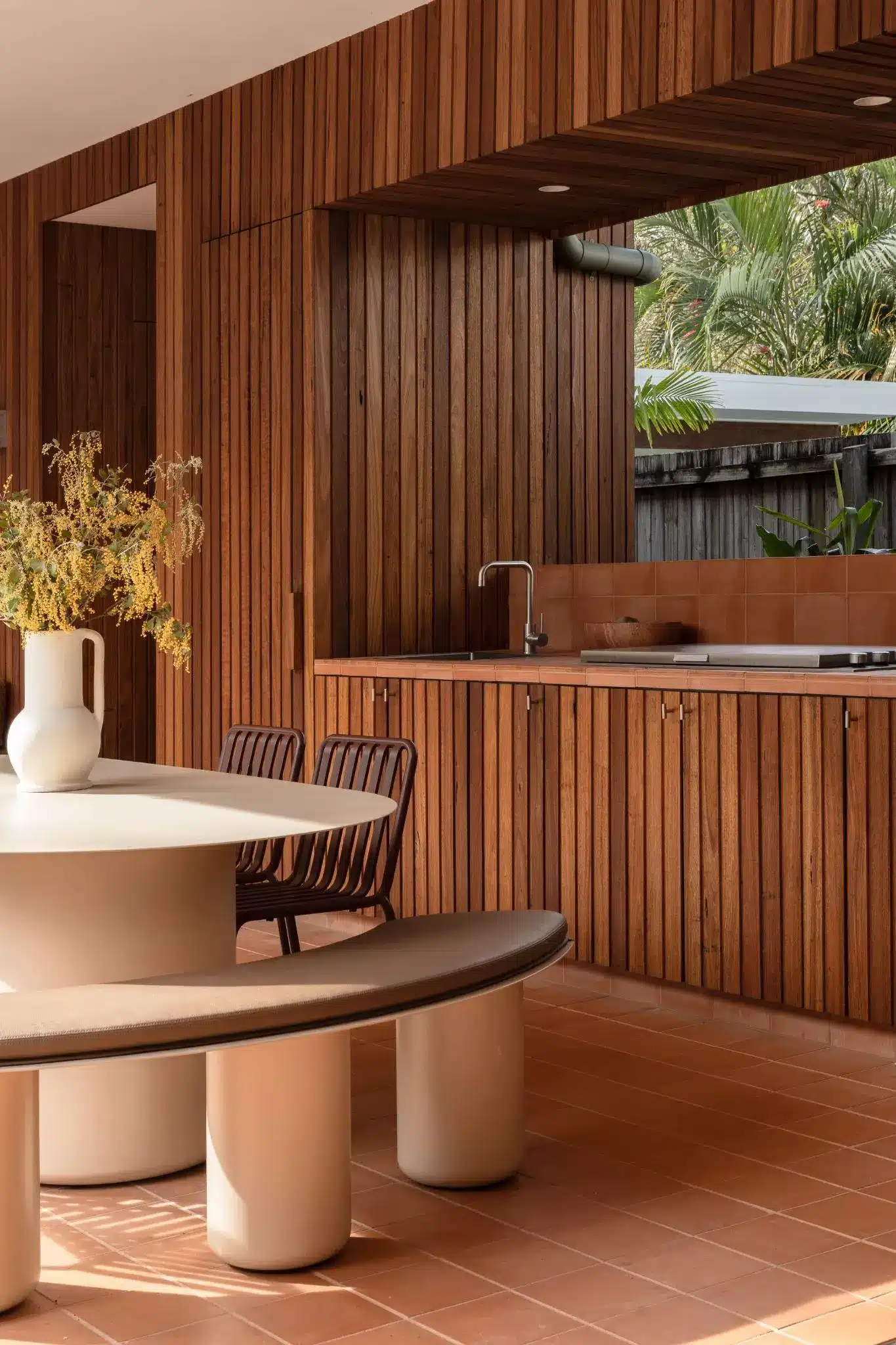 Wood-paneled outdoor kitchen with round table and chairs, surrounded by tropical plants
