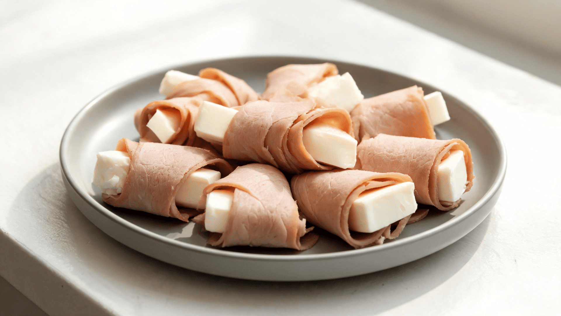 turkey roll ups with string cheese arranged on a gray plate for a high protein snack
