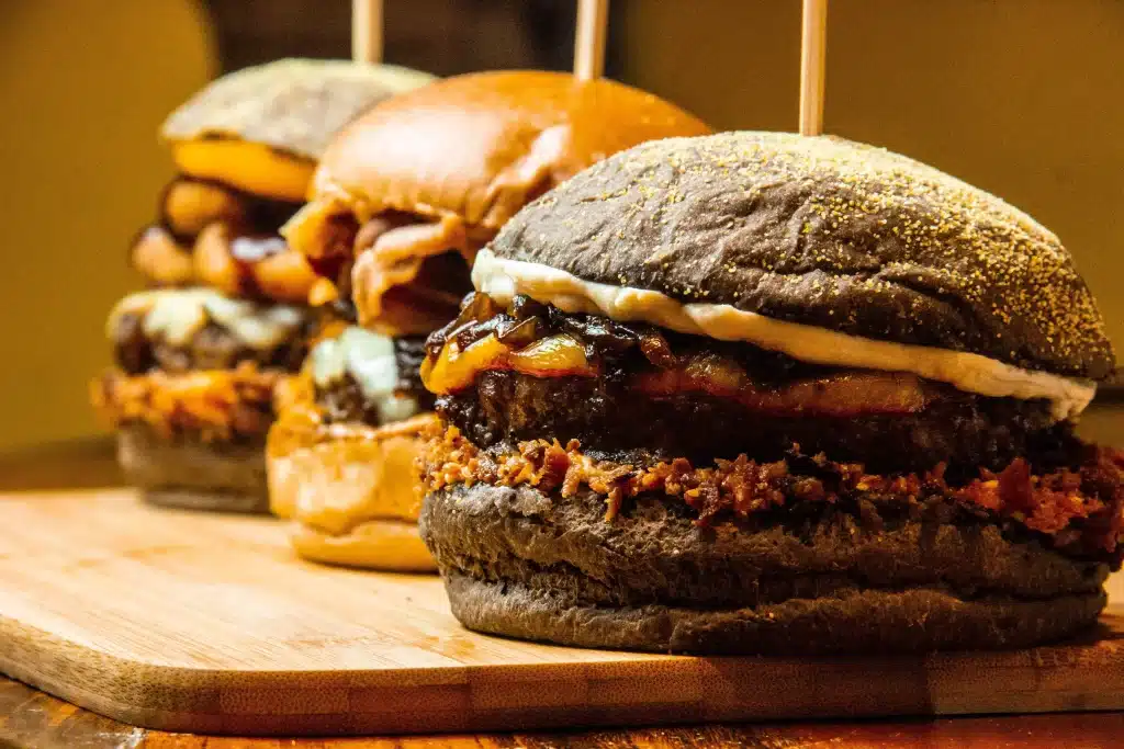 Three gourmet burgers with varied toppings on wooden board in cozy restaurant setting