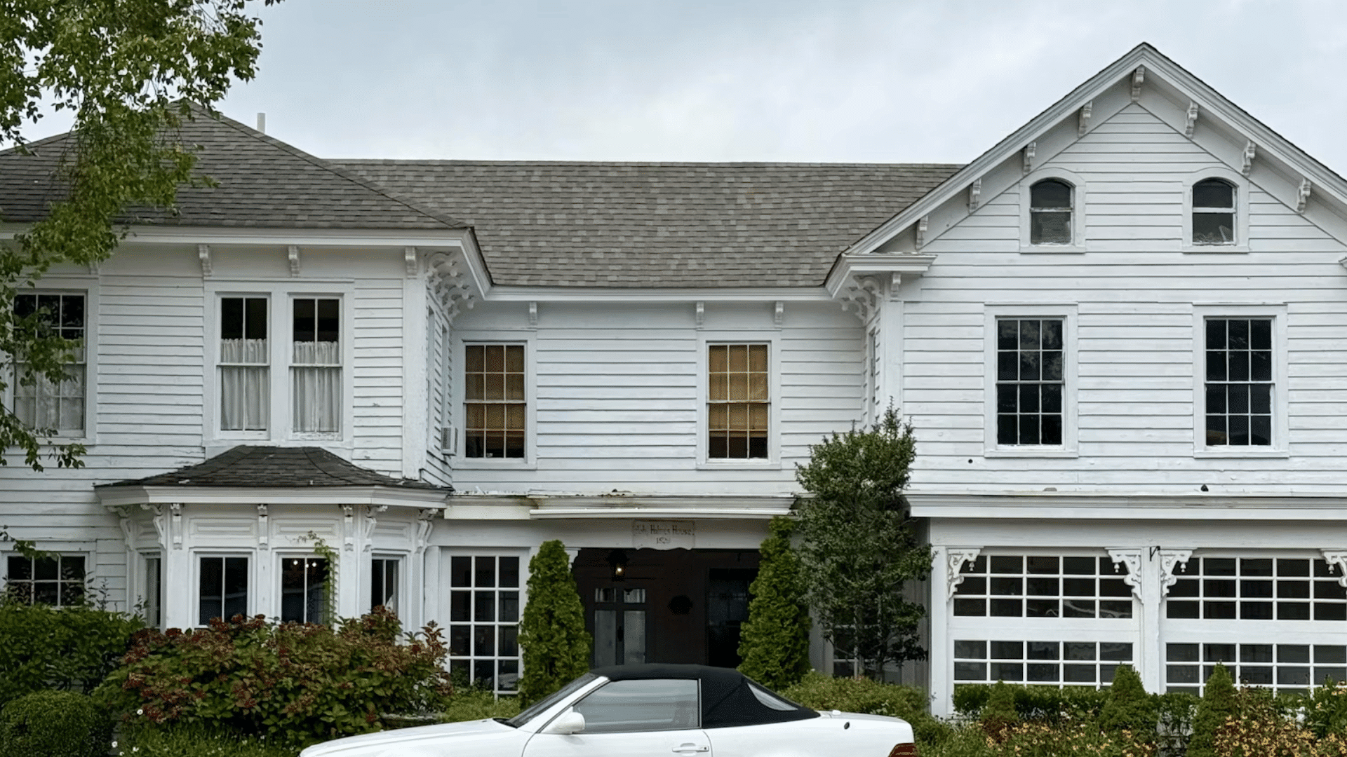 white wooden house with large windows and a white car parked in front of a landscaped garden area