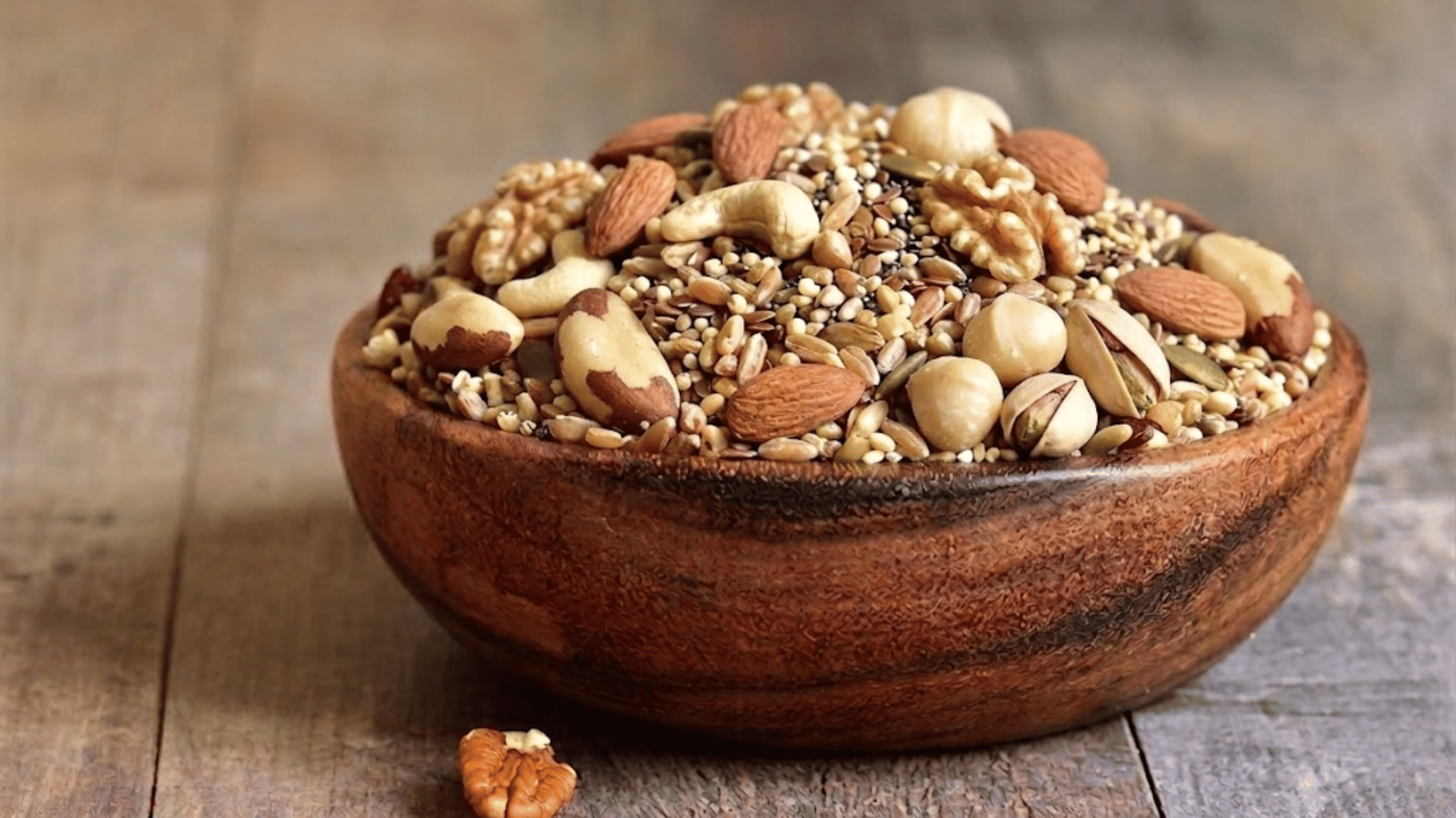 wooden bowl filled with mixed nuts and dried fruit including almonds cashews pecans raisins and golden raisins on table