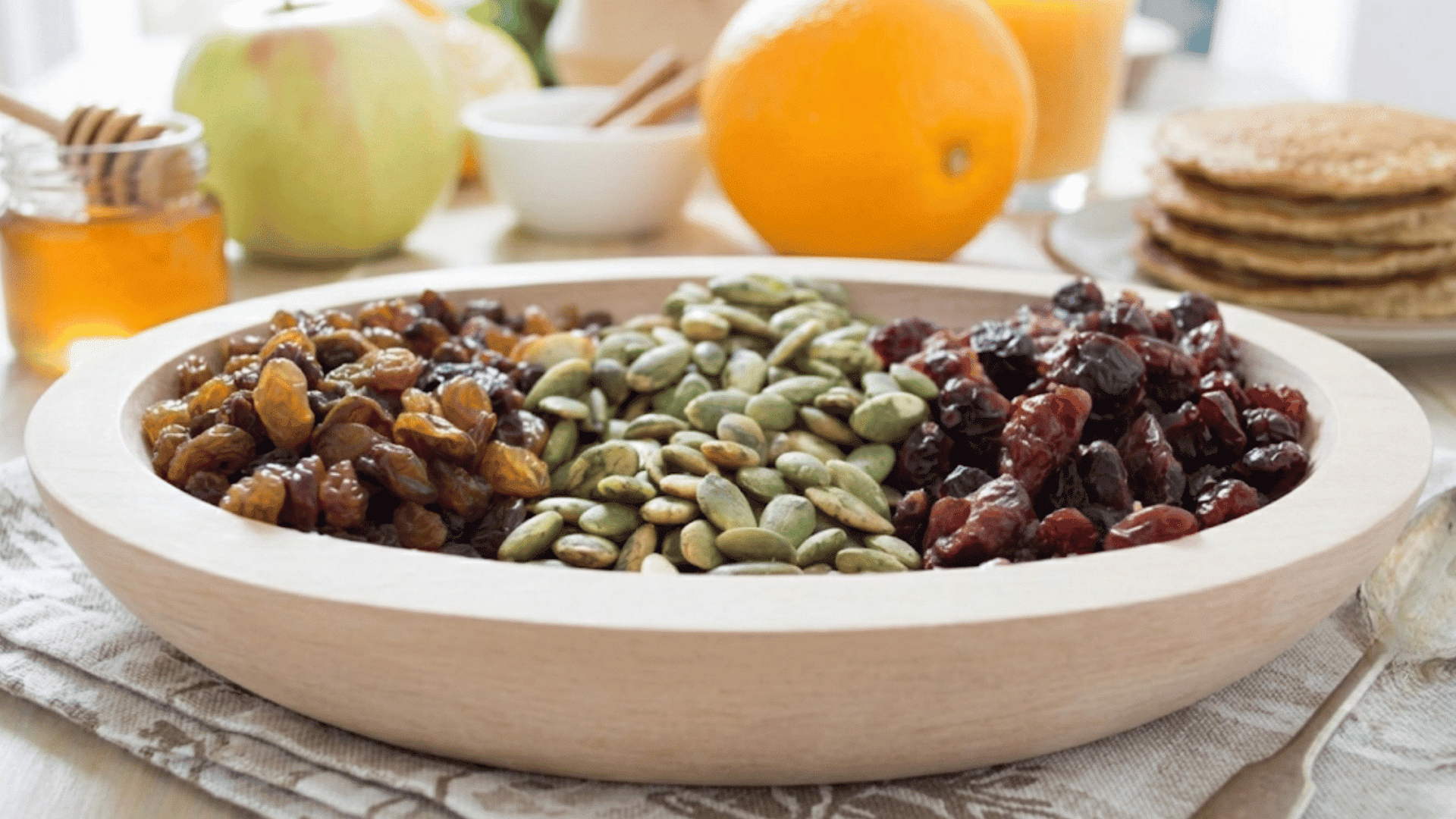 wooden bowl filled with pumpkin seeds raisins and dried cranberries arranged as a healthy snack with fresh fruit in background (2)