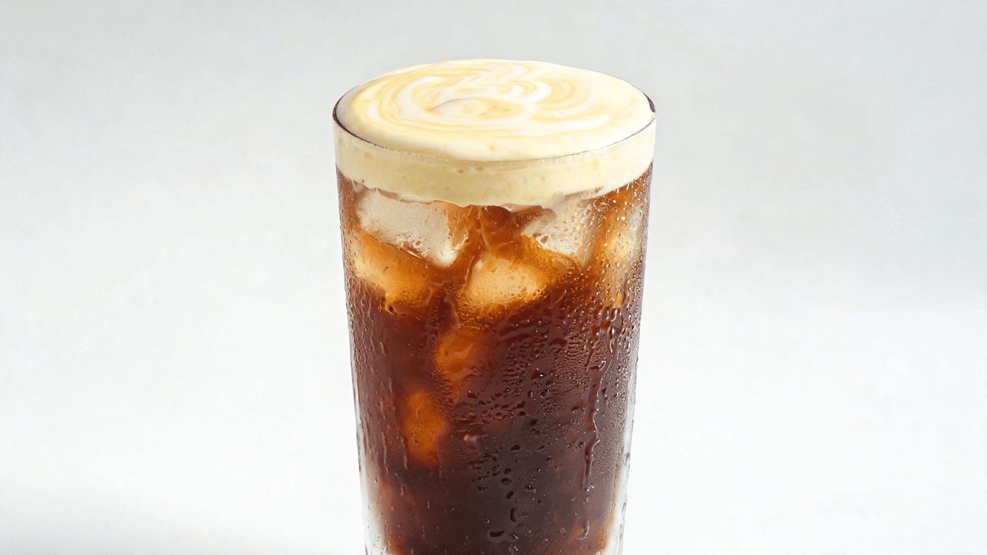 Iced egg coffee with creamy foam topping served in a tall glass with coffee layers and ice cubes.