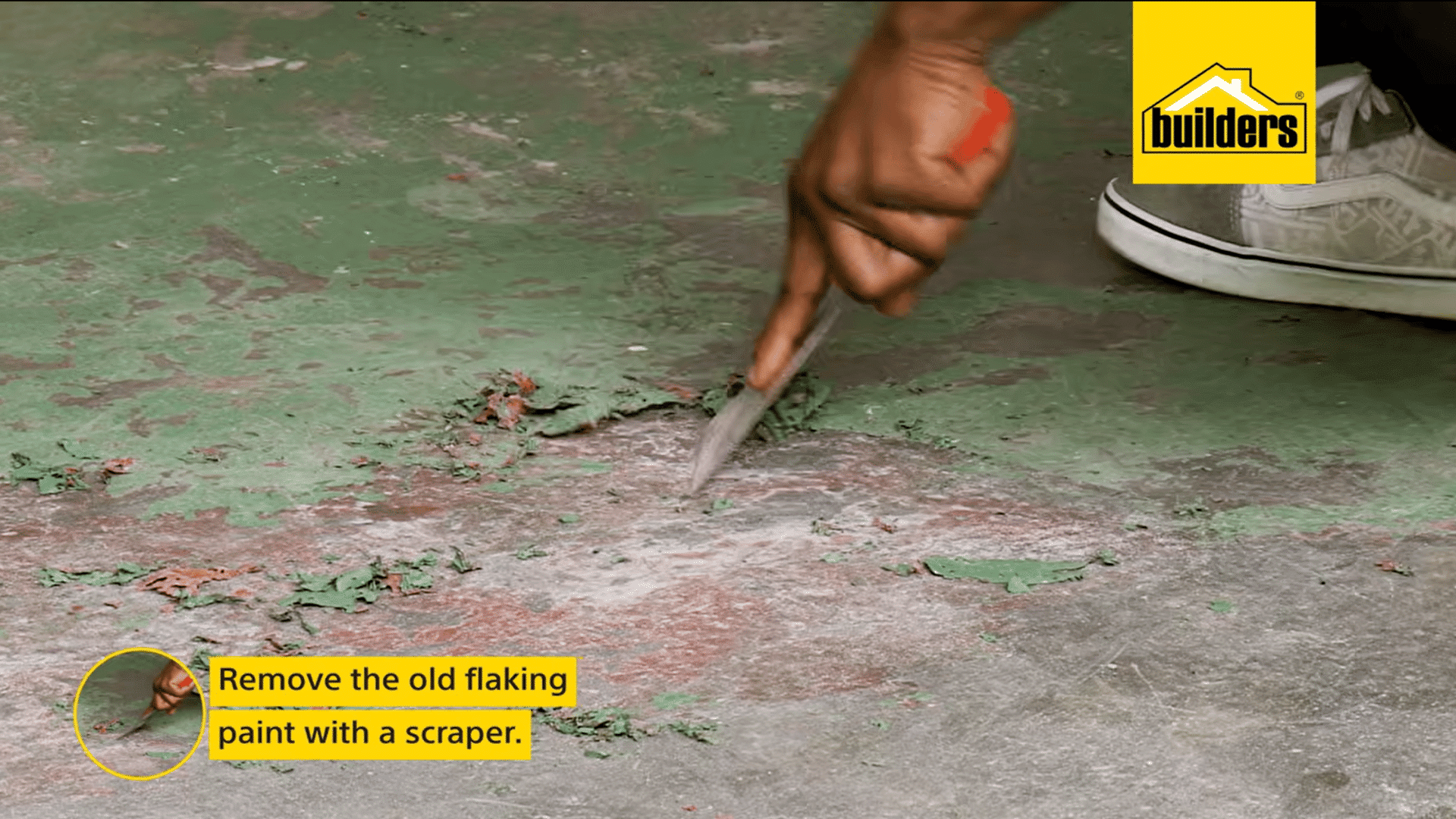 a hand uses a scraper to remove old flaking green paint from a concrete floor preparing the surface for repainting