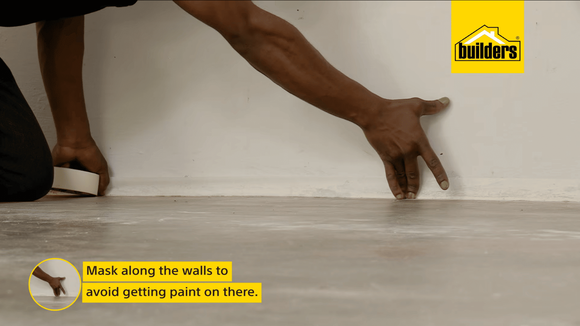 a person applies masking tape along the base of a wall to protect the surface from paint while preparing a concrete floor