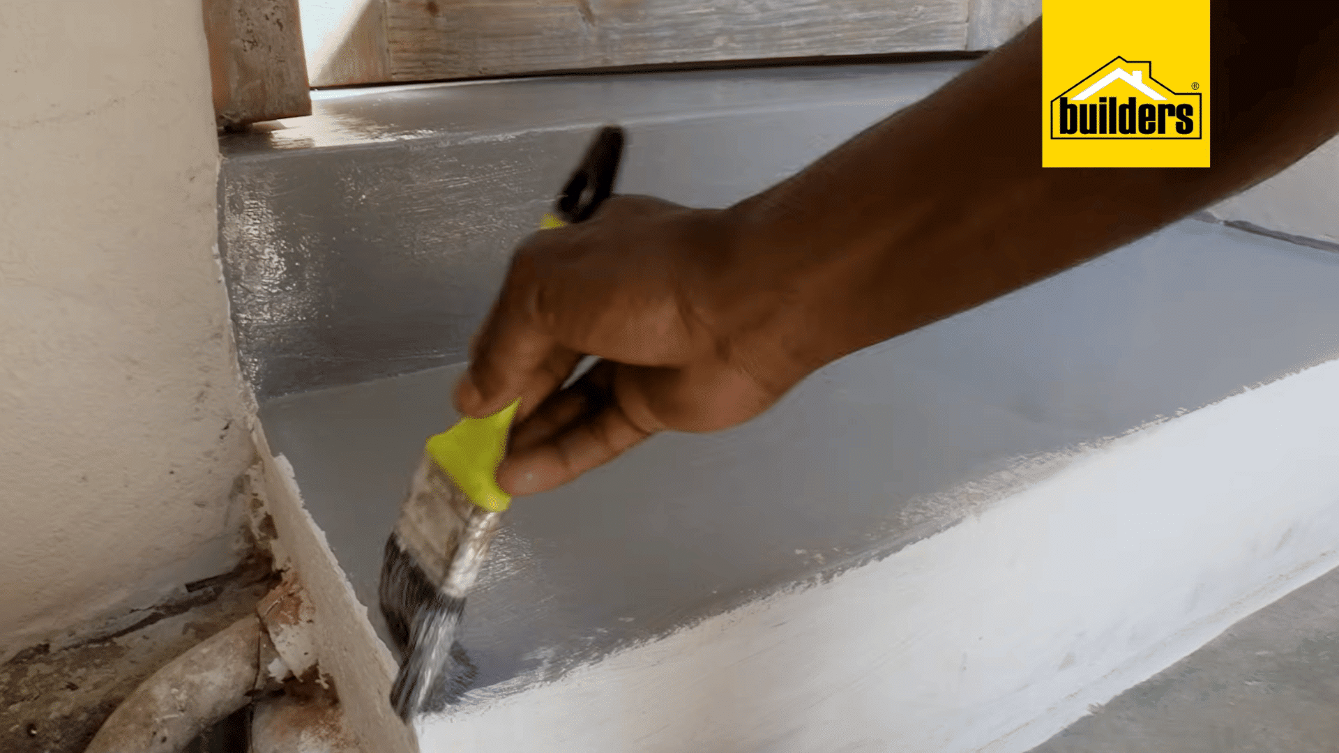 a person uses a paintbrush to apply grey floor paint along the edge of a concrete step for neat coverage around corners and edges