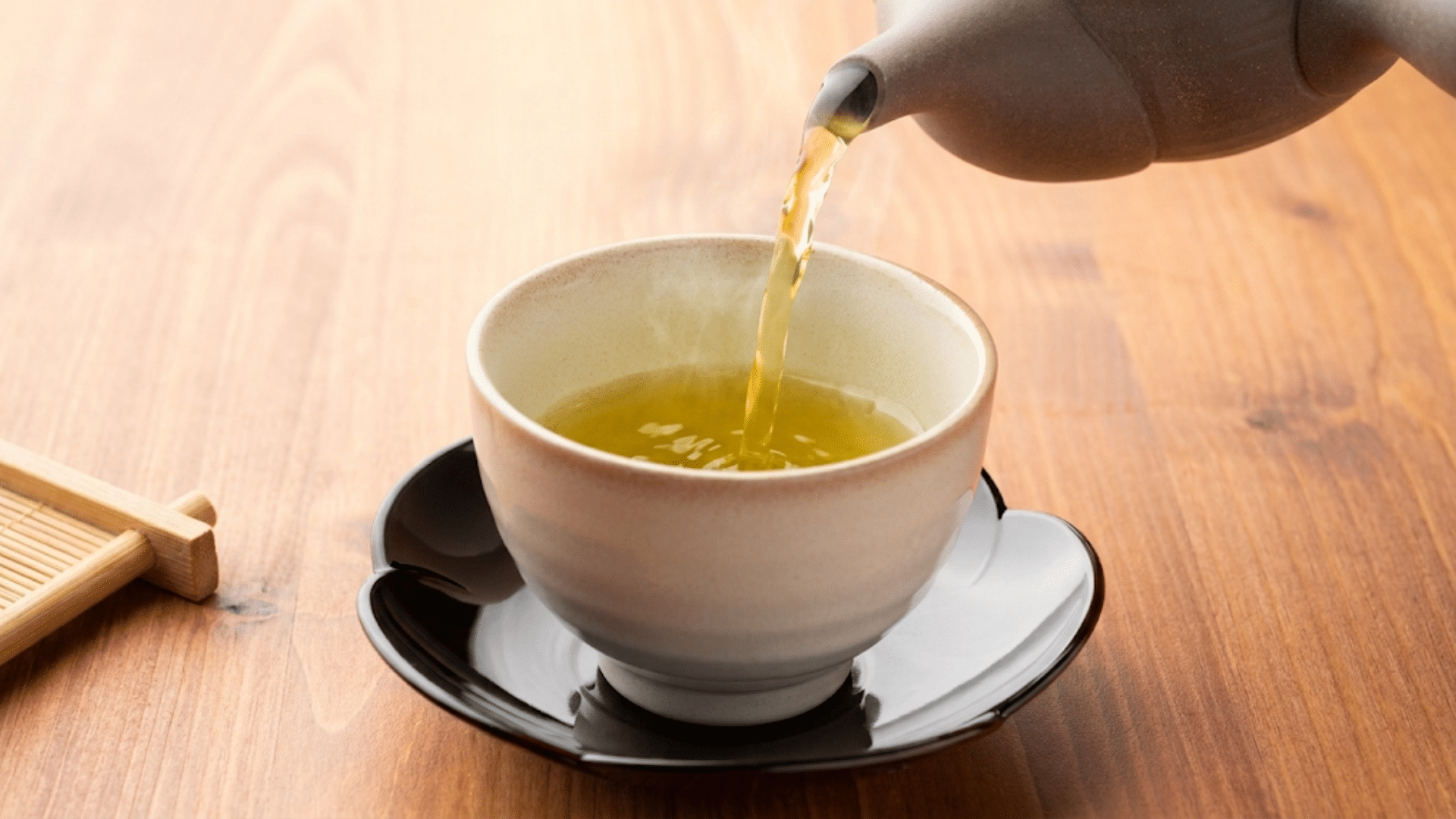 a teapot pouring what is the best green tea to drink into a ceramic cup on a wooden table for a relaxing tea experience