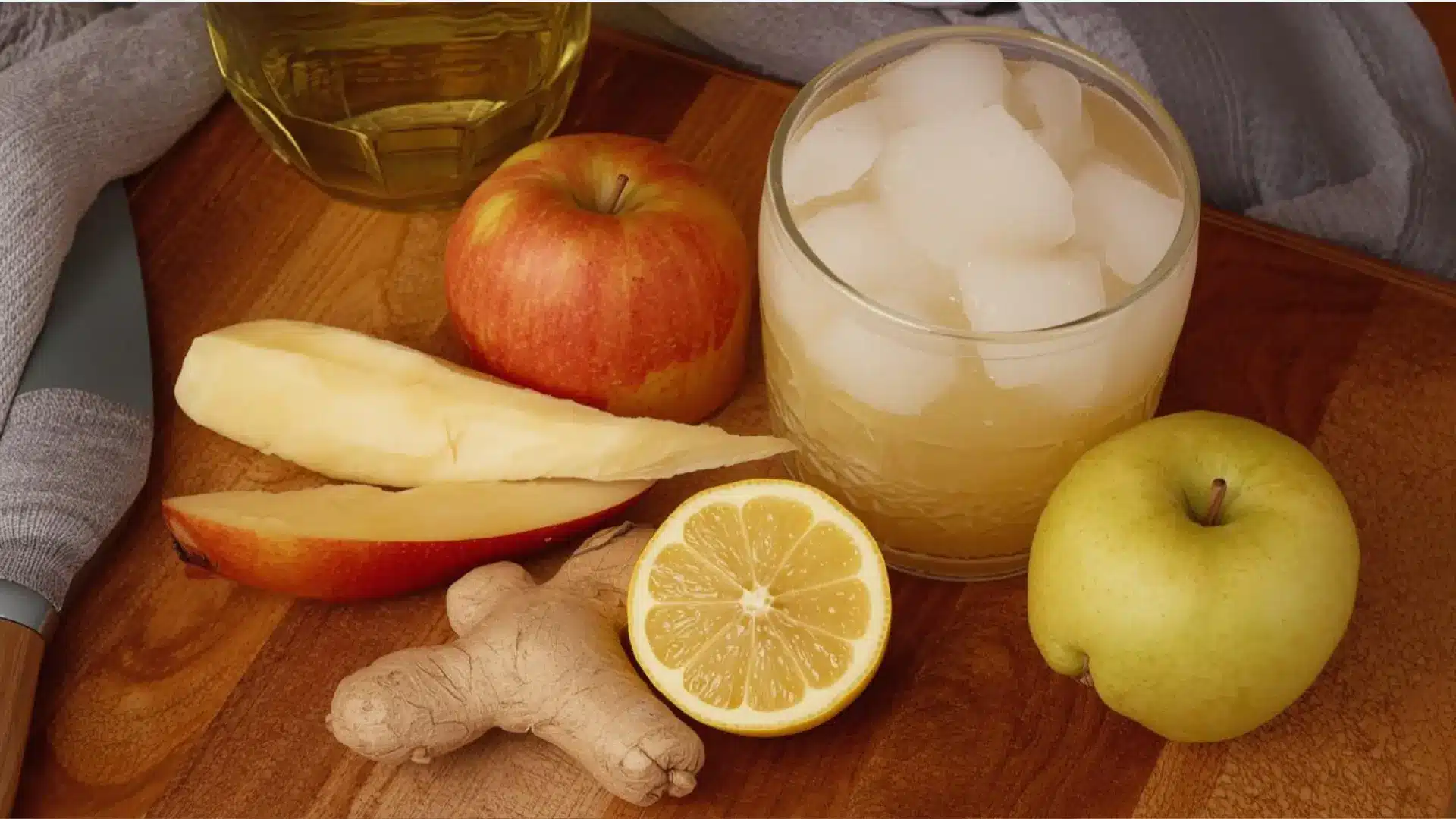 apple lemon ginger juice with ice beside fresh apples lemon slices and ginger on a wooden board