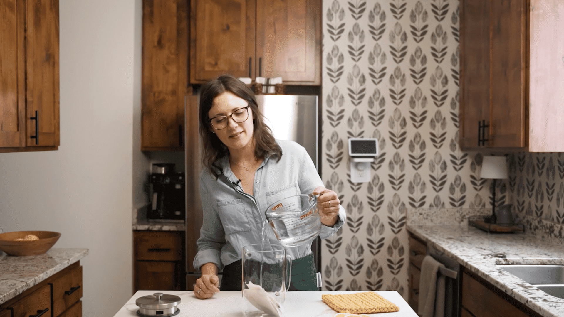 A woman pours cold water into a glass pitcher with tea bags while making homemade iced tea in her kitchen