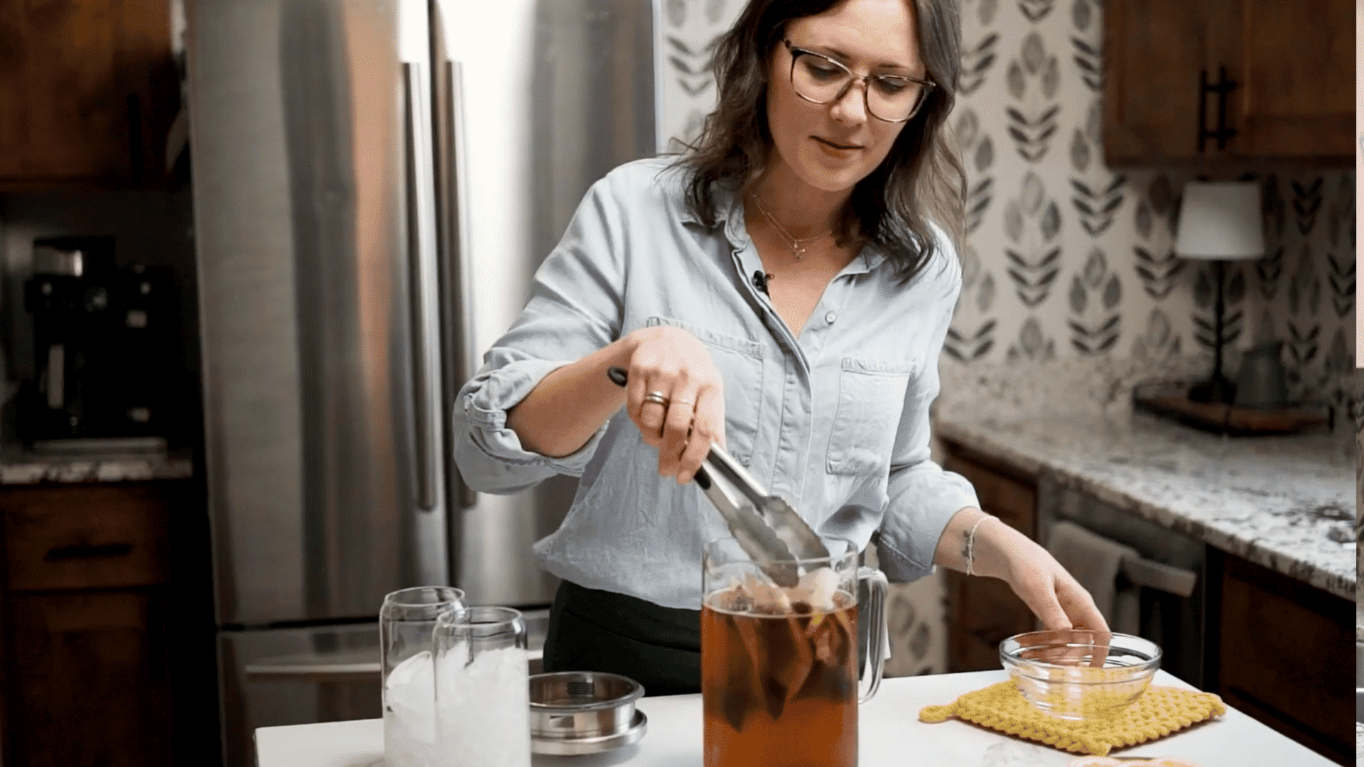 A woman removes tea bags from a pitcher of cold brew iced tea using kitchen tongs