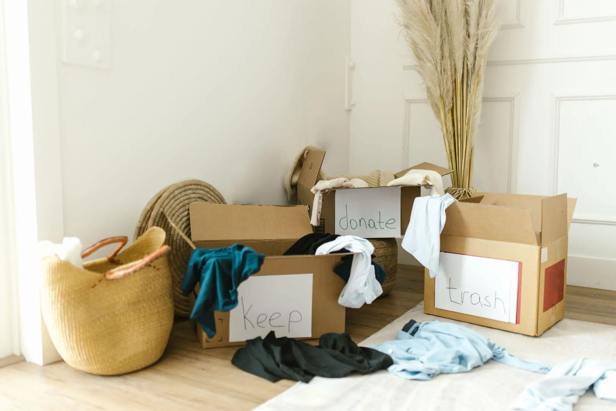 Cardboard boxes labeled keep, donate, and trash filled with clothes in bright room