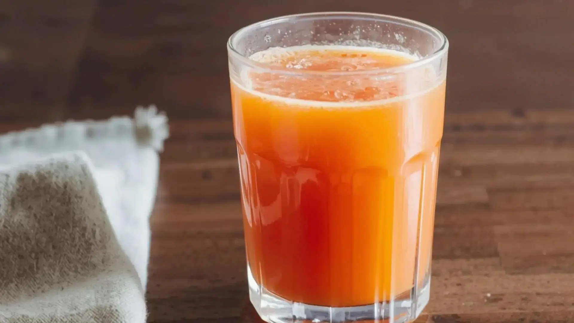 fresh carrot orange juice in a clear glass on a wooden table beside a folded cloth (1)