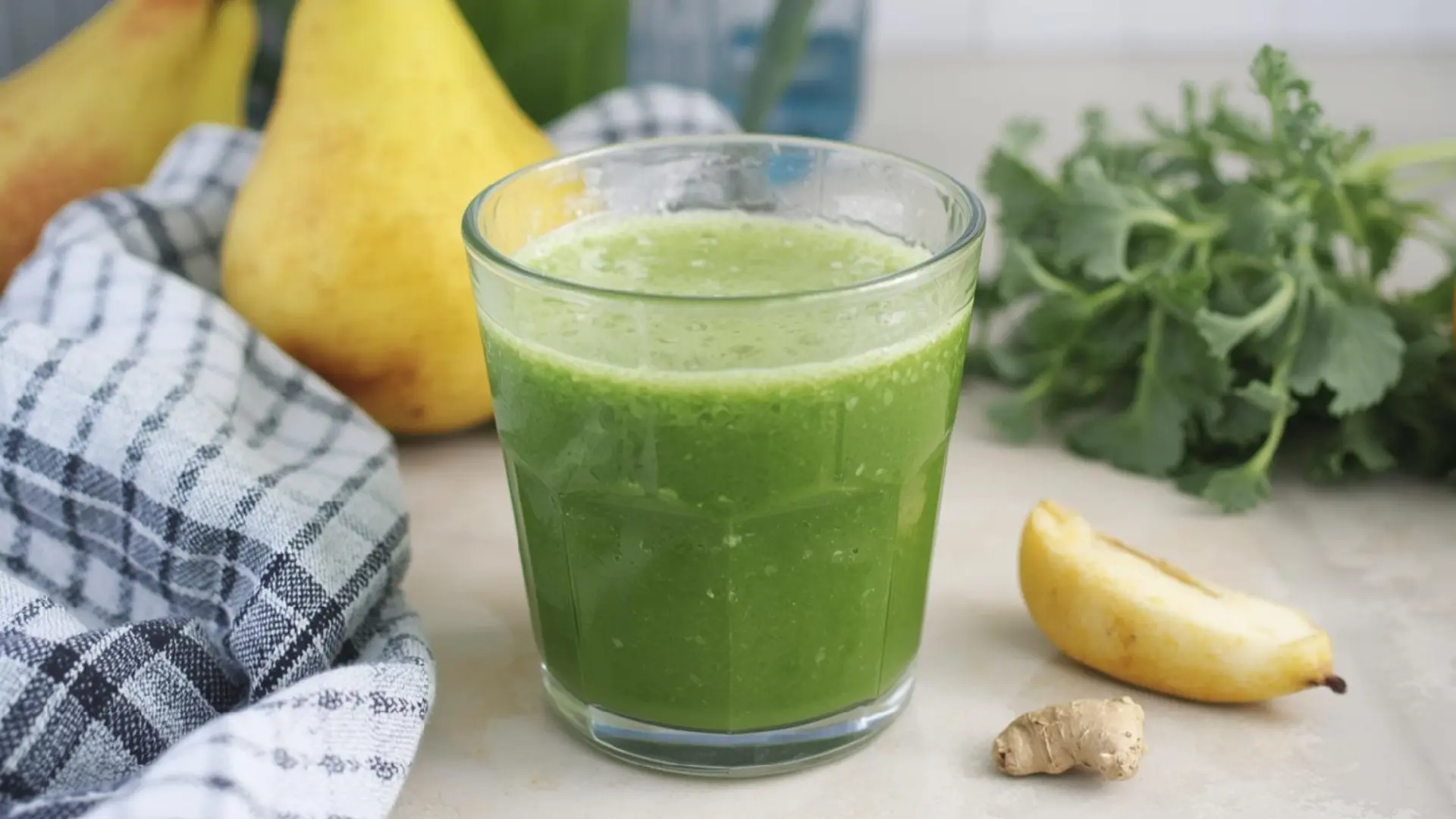 green pear spinach juice in a glass with fresh pears ginger and greens on a light kitchen counter