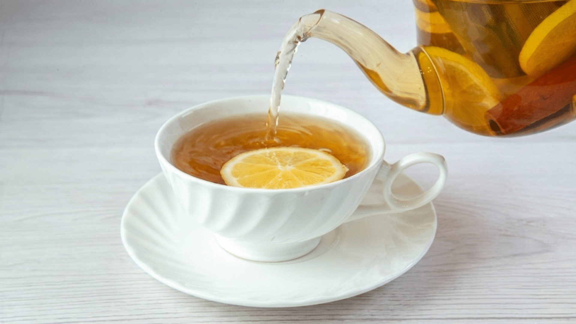 herbal tea with a lemon slice being poured from a glass teapot into a white cup on a table
