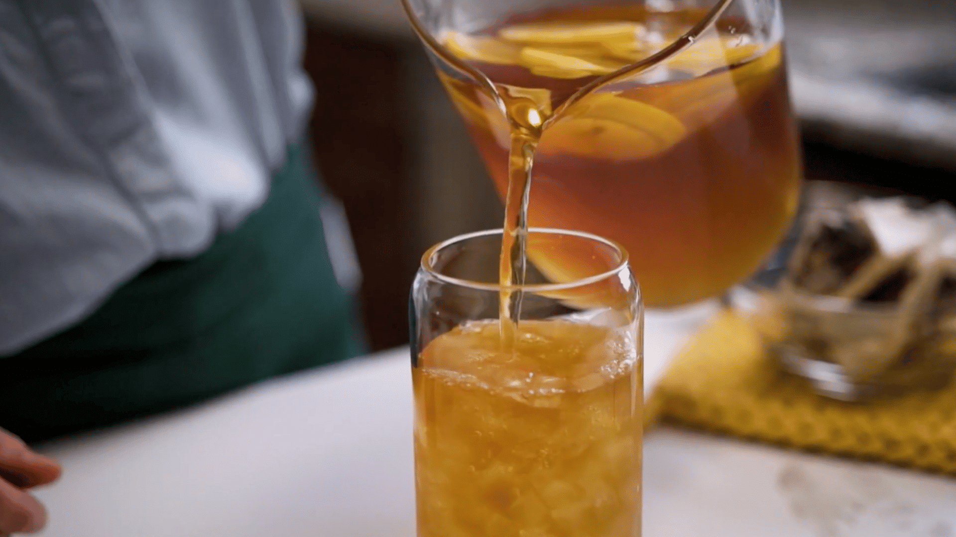 Homemade lemon iced tea being poured from a glass pitcher into an ice-filled serving glass.