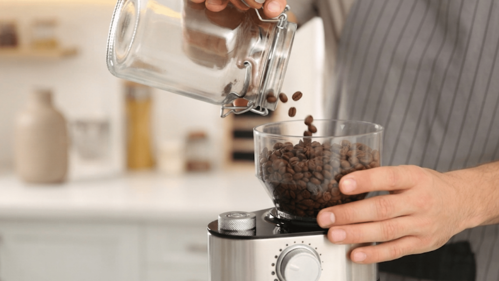 person pouring coffee beans into grinder container for preparing fresh ground coffee at home kitchen setting