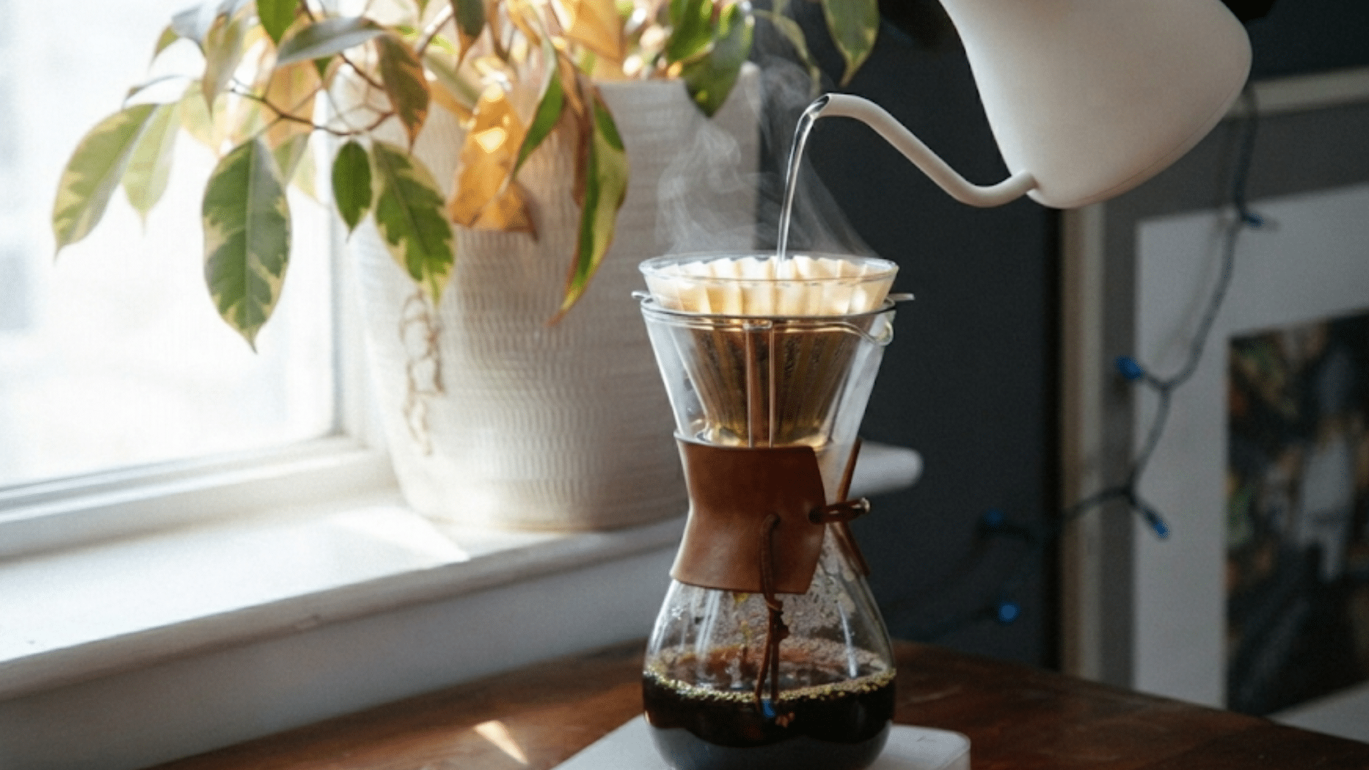 pour over coffee brewing setup with glass dripper kettle and fresh coffee beside window in home kitchen setting