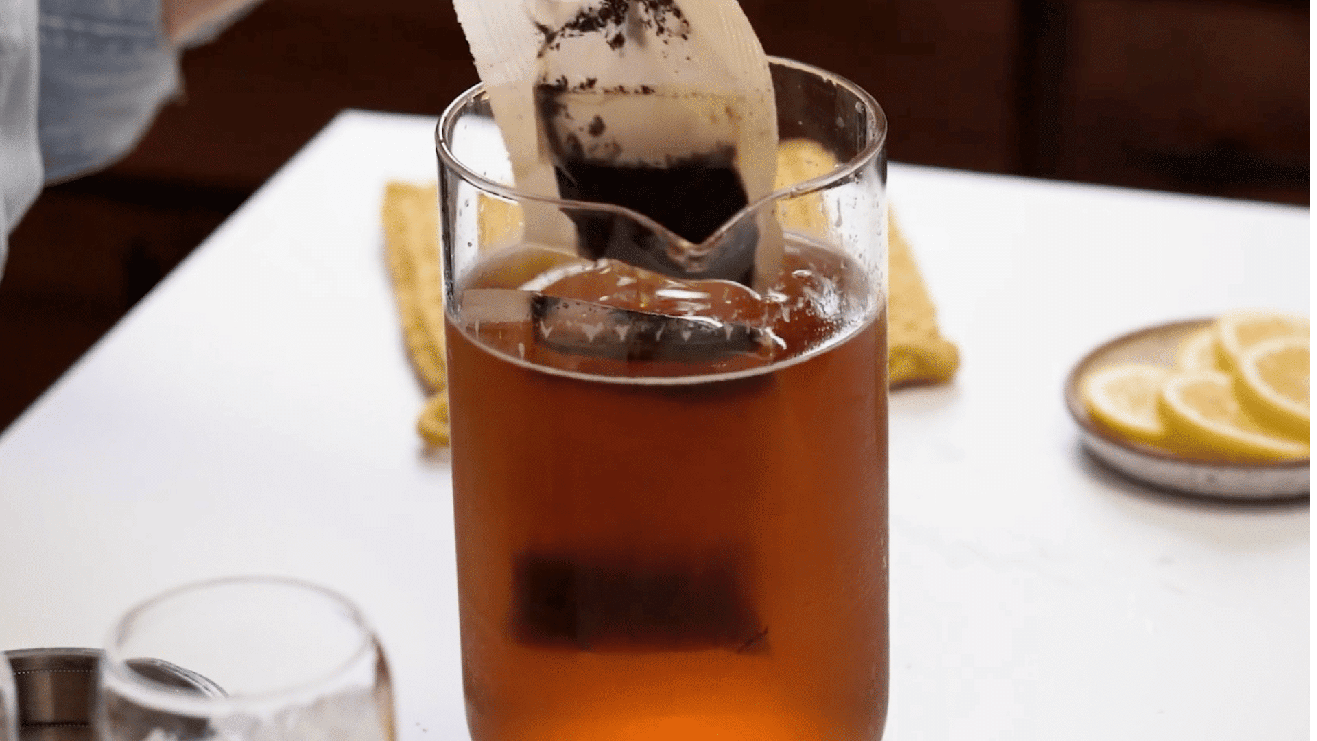 Tea bags being lifted from a glass pitcher of cold brew iced tea with lemon slices ready for serving.
