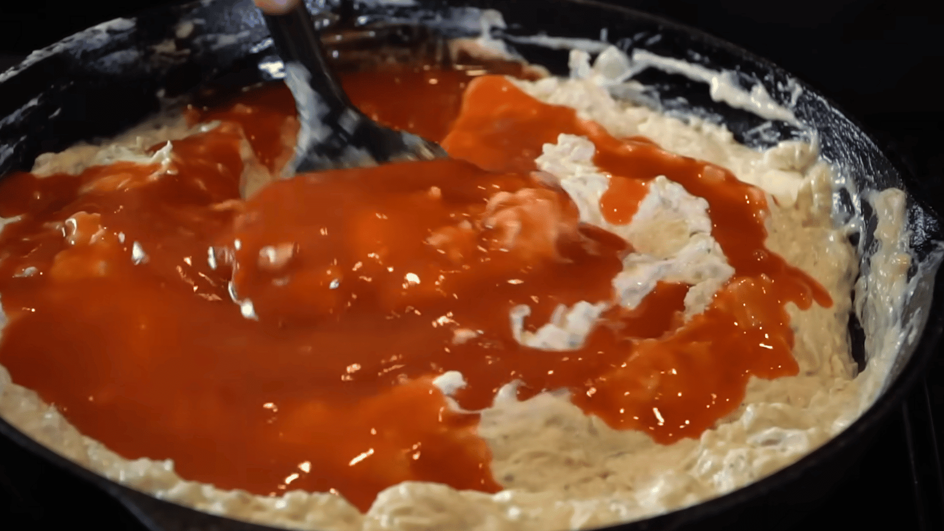 mixing hot sauce and shredded cheese into buffalo chicken dip