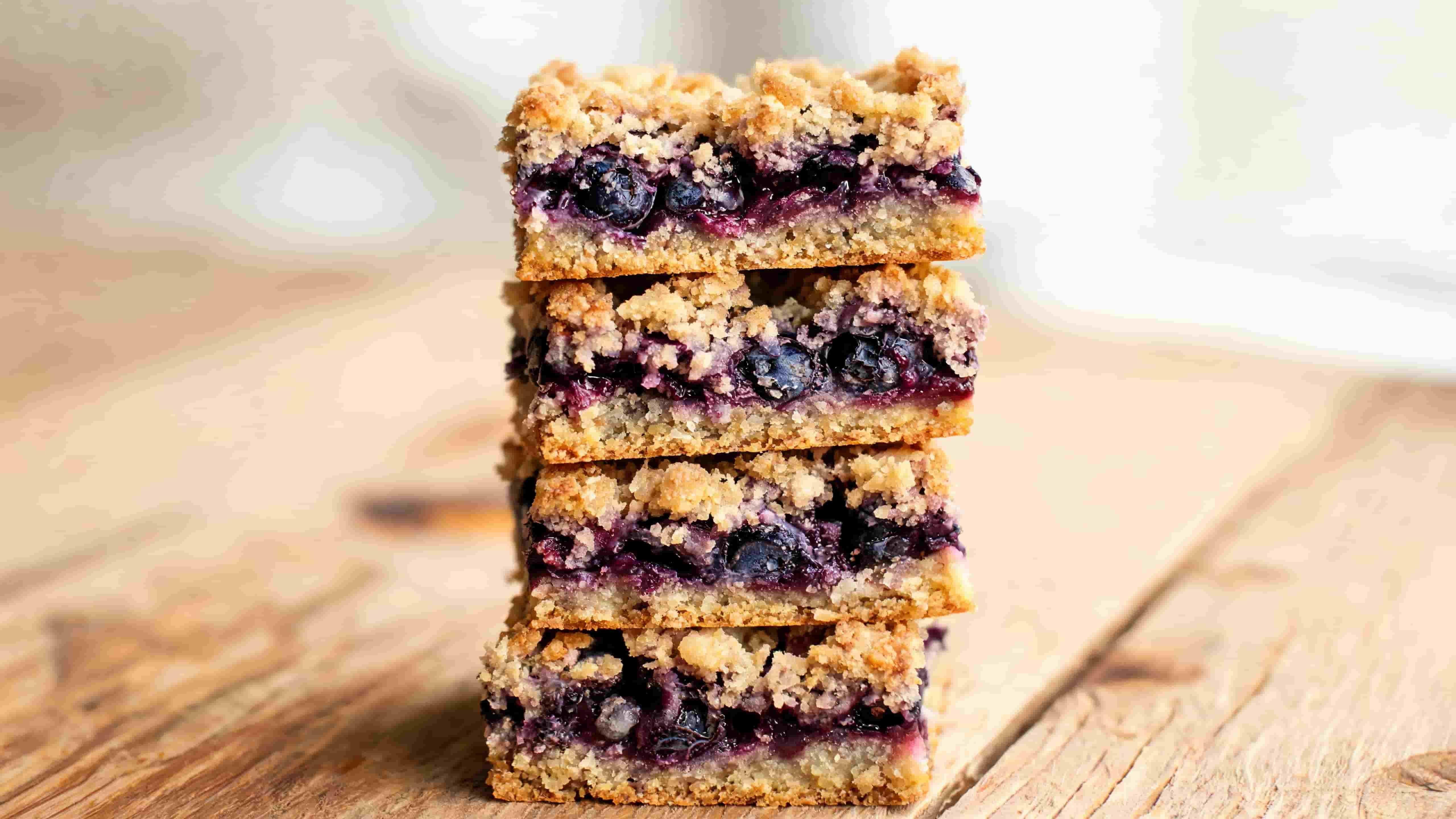 stacked blueberry crumble bars with visible berry layers and golden crumb topping on parchment over wooden surface