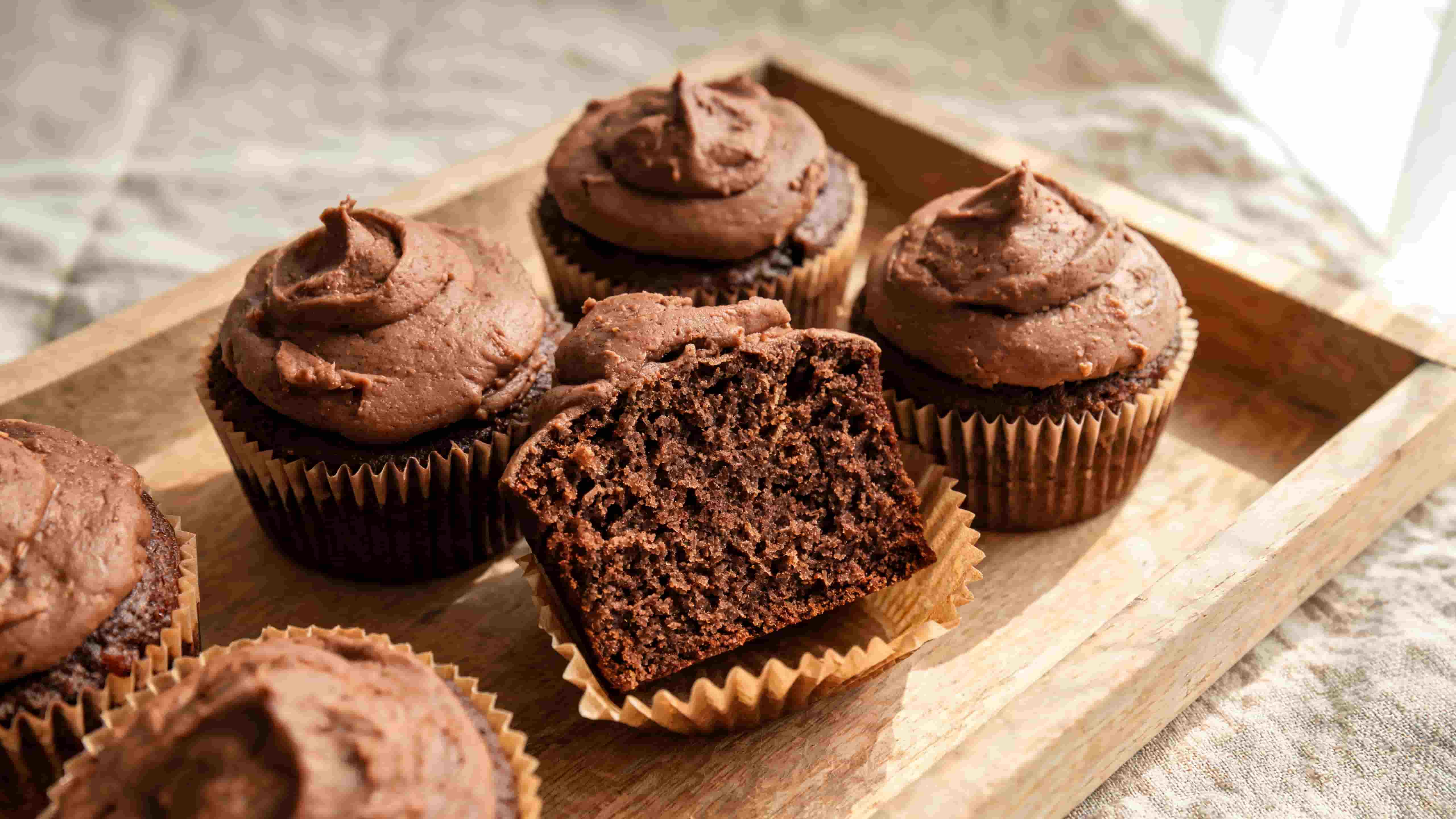 chocolate cupcakes topped with creamy chocolate frosting arranged on a wooden serving tray with one cupcake cut open