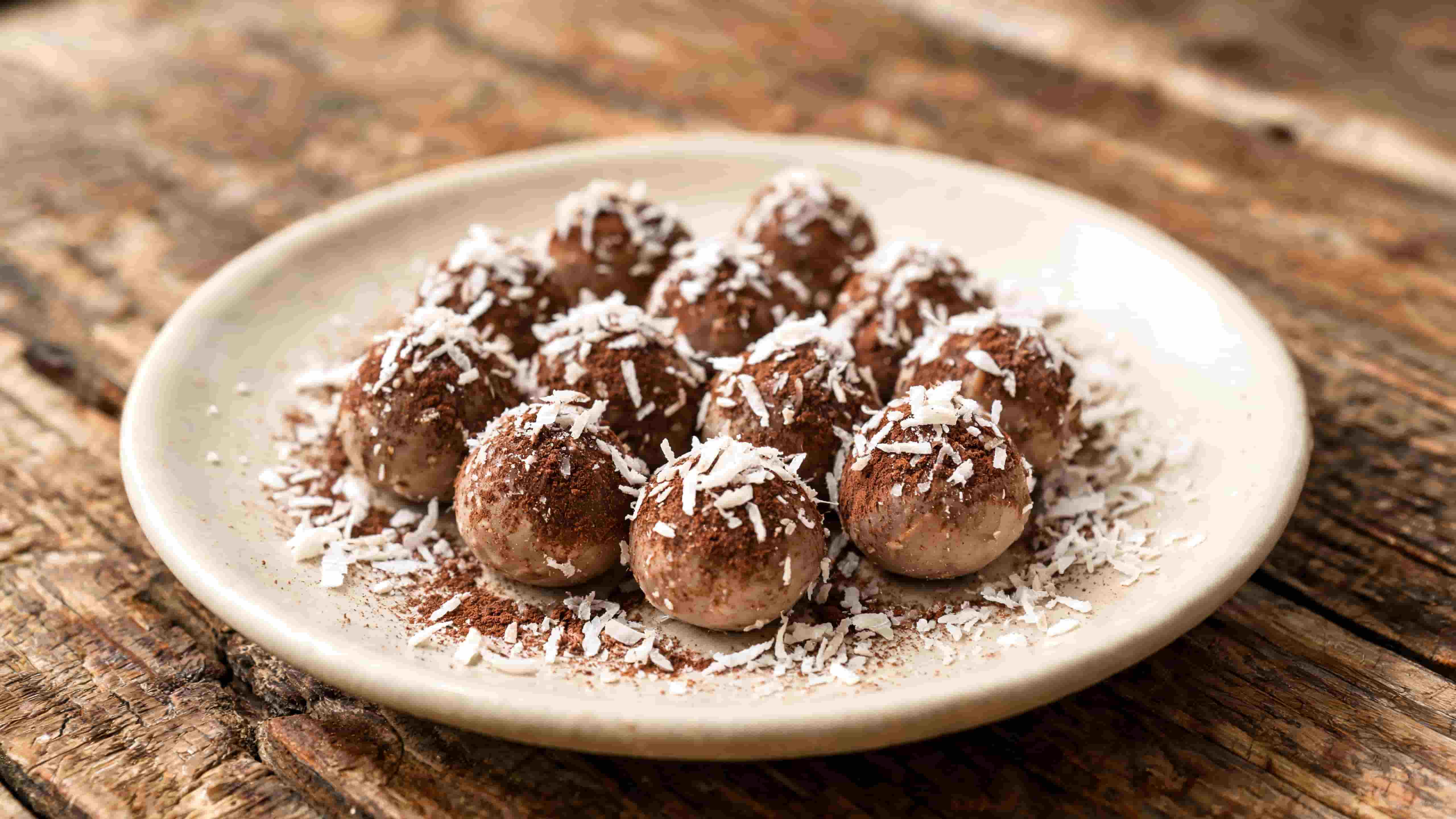 chocolate coconut energy bites dusted with cocoa and shredded coconut on a white plate