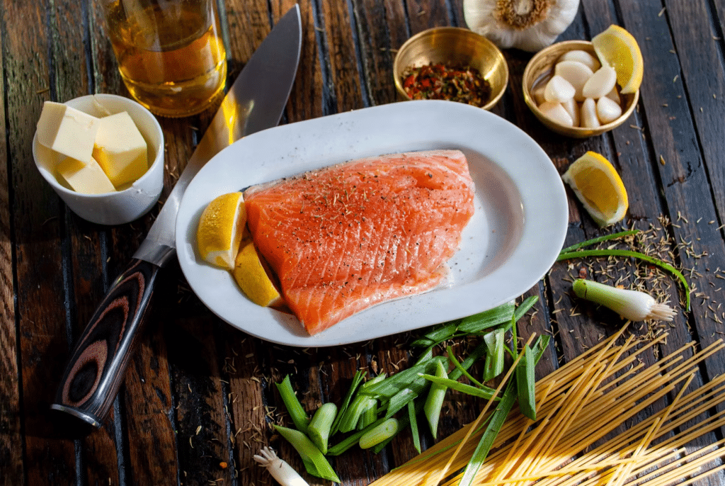 Raw salmon fillet with lemon and herbs on a white plate, surrounded by garlic and green onions