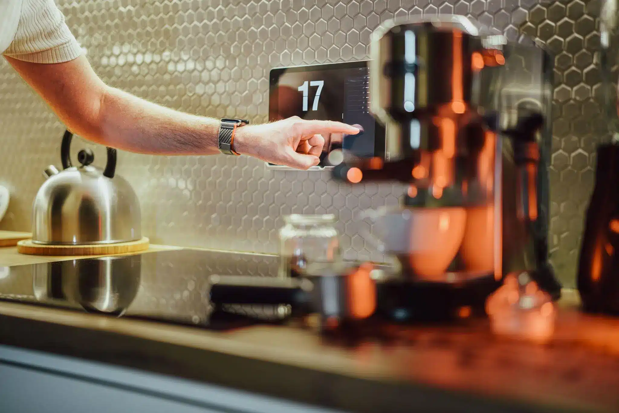 Hand adjusting touch screen in modern kitchen with hexagonal backsplash and stainless steel kettle