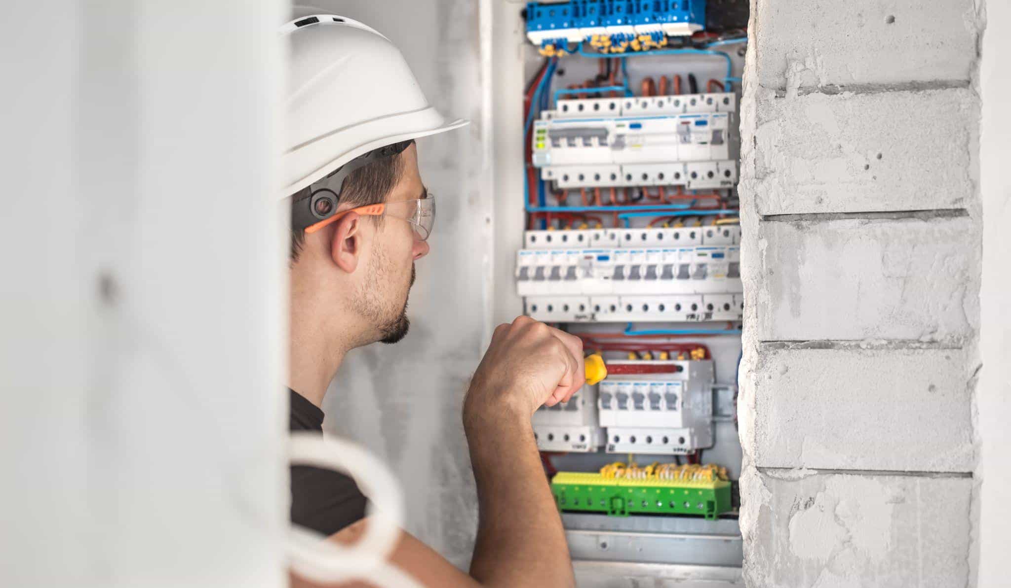 Electrician with hard hat working on breaker panel in unfinished building interior
