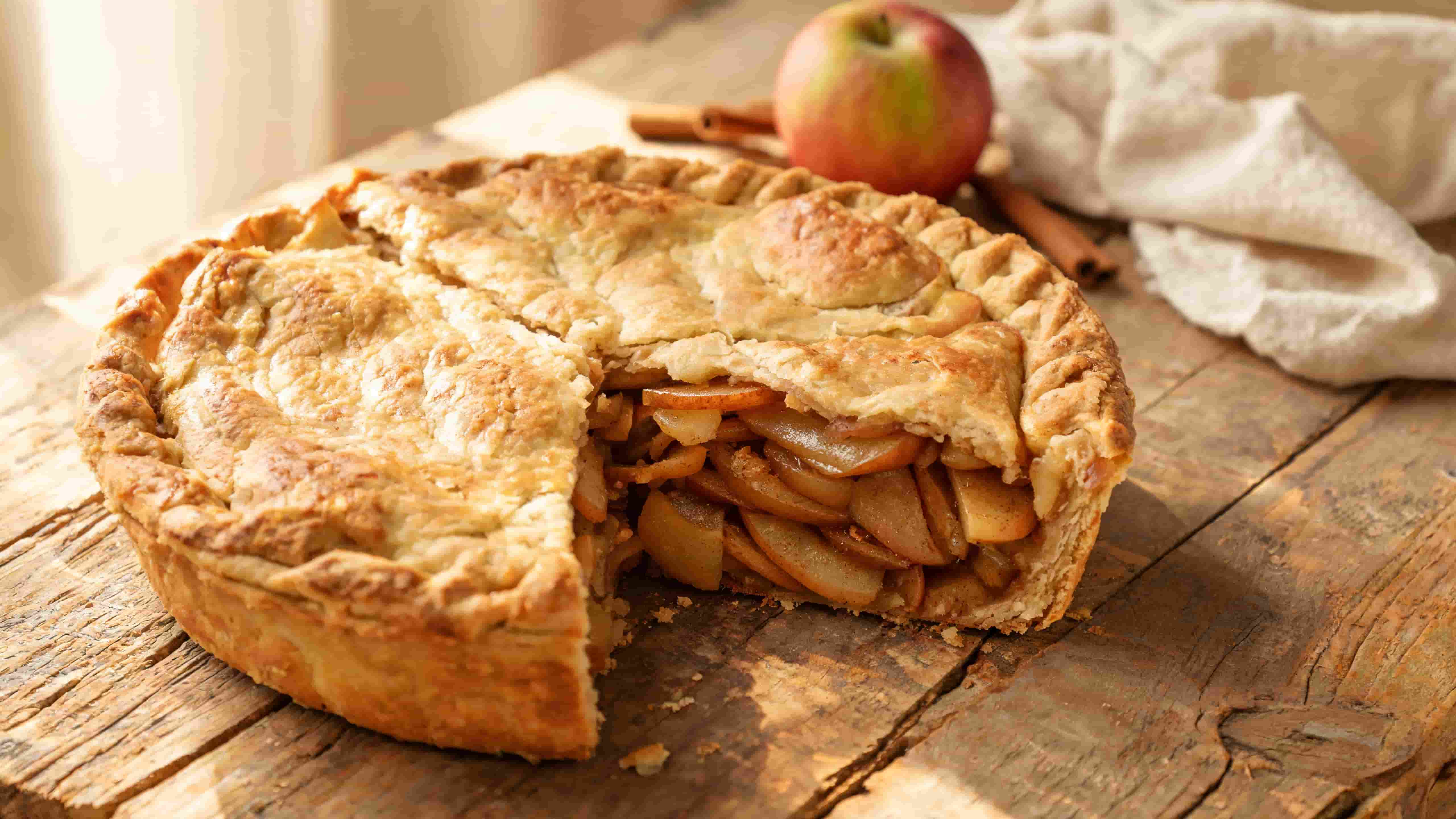 homemade apple pie on plate with slice removed showing layered spiced apple filling and flaky crust on rustic table