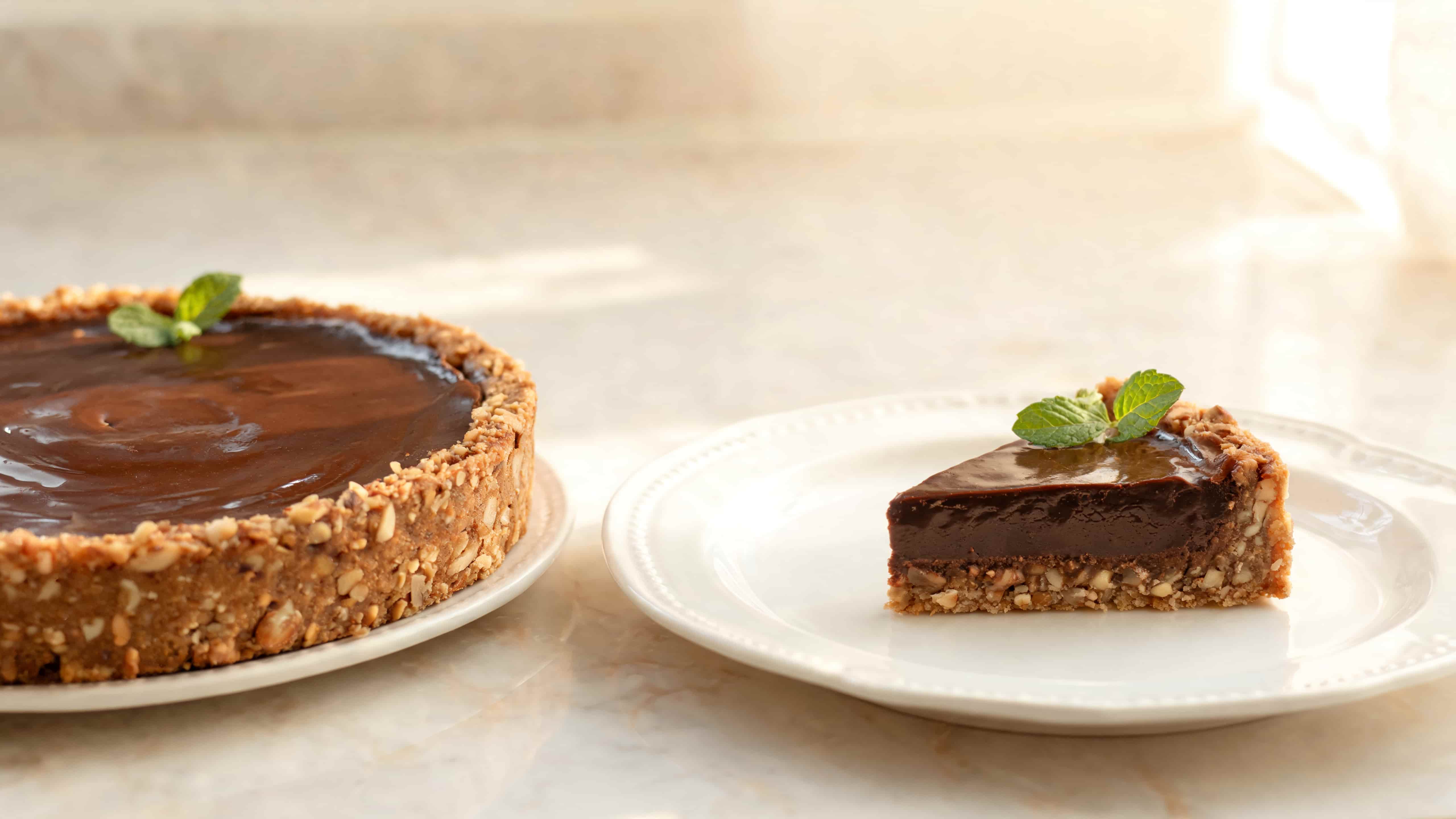 rich chocolate tart with a slice removed showing dense filling and nutty crust on white plates in soft natural light