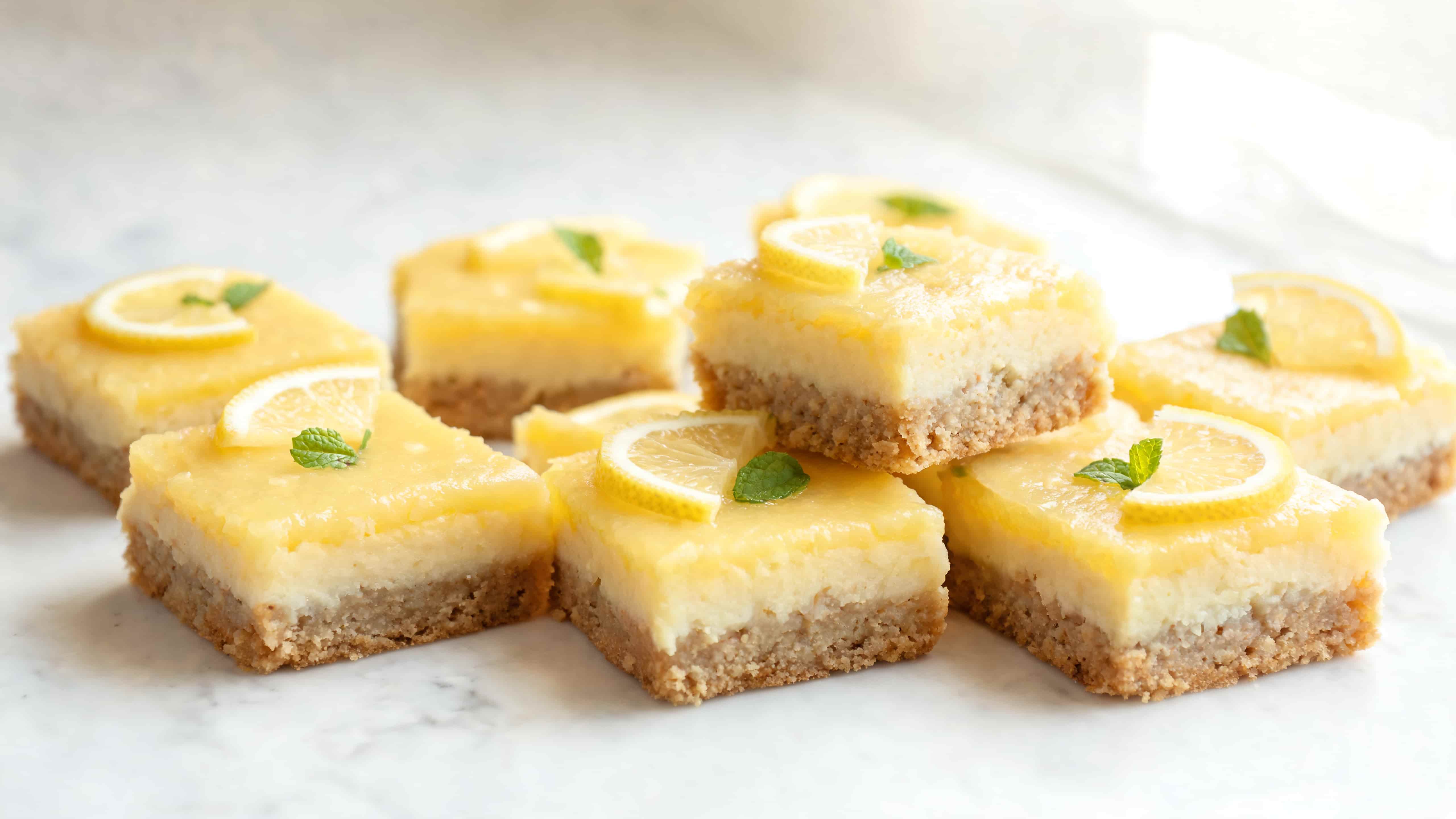 stacked lemon dessert bars with glaze and lemon slices on top arranged on a light marble surface