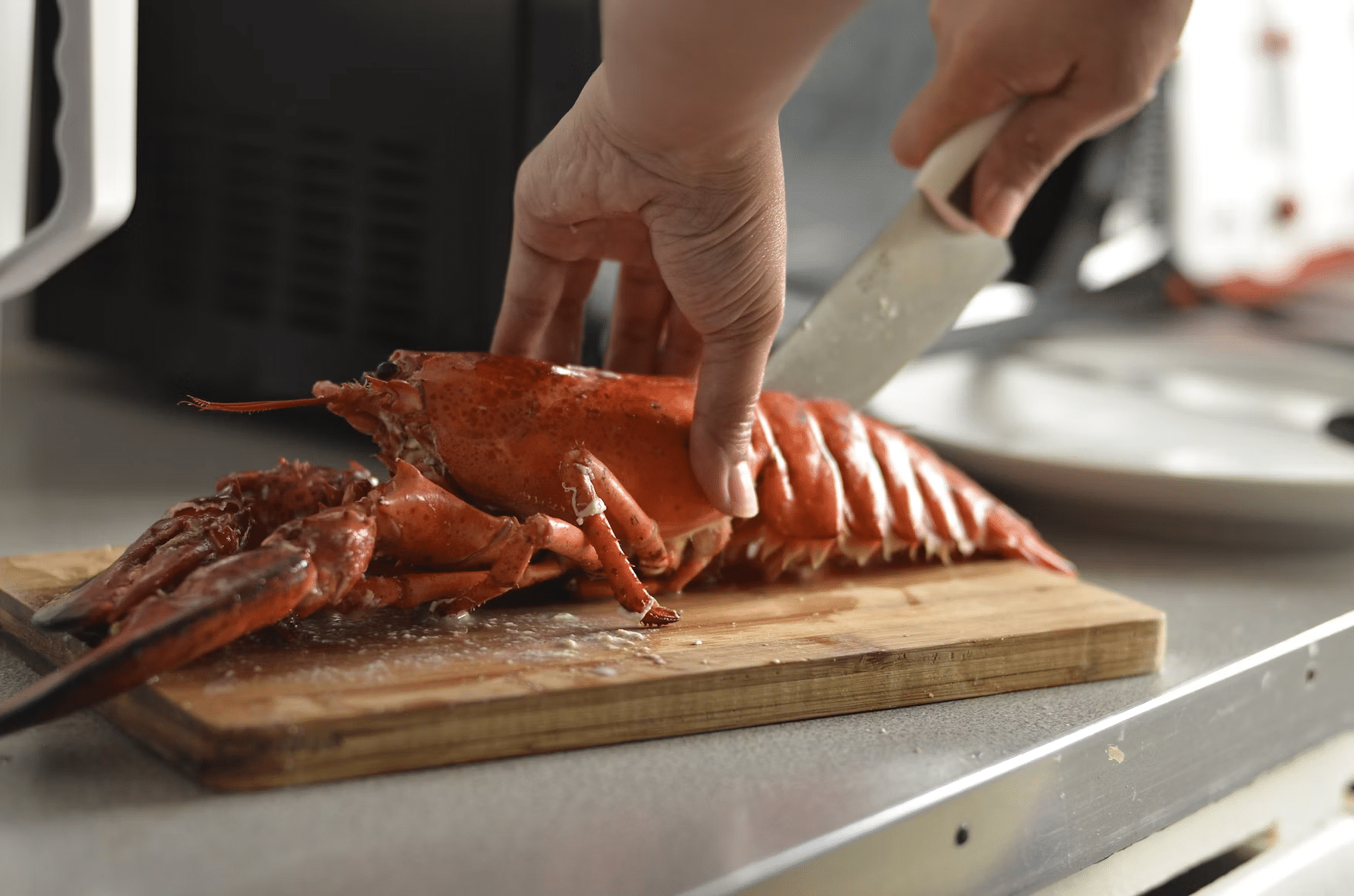Cutting cooked lobster with knife on wooden board in a kitchen setting