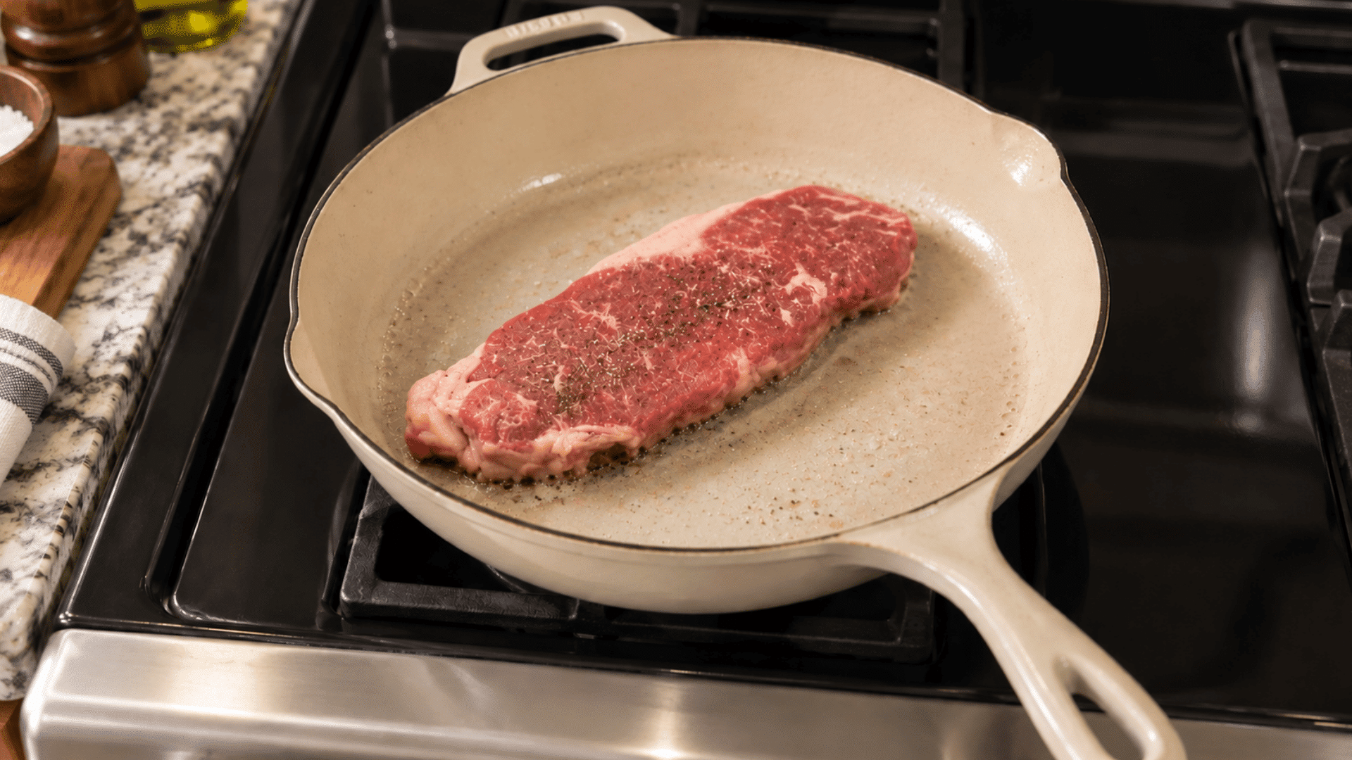 Raw seasoned steak cooking in a beige skillet on a stovetop with minimal oil