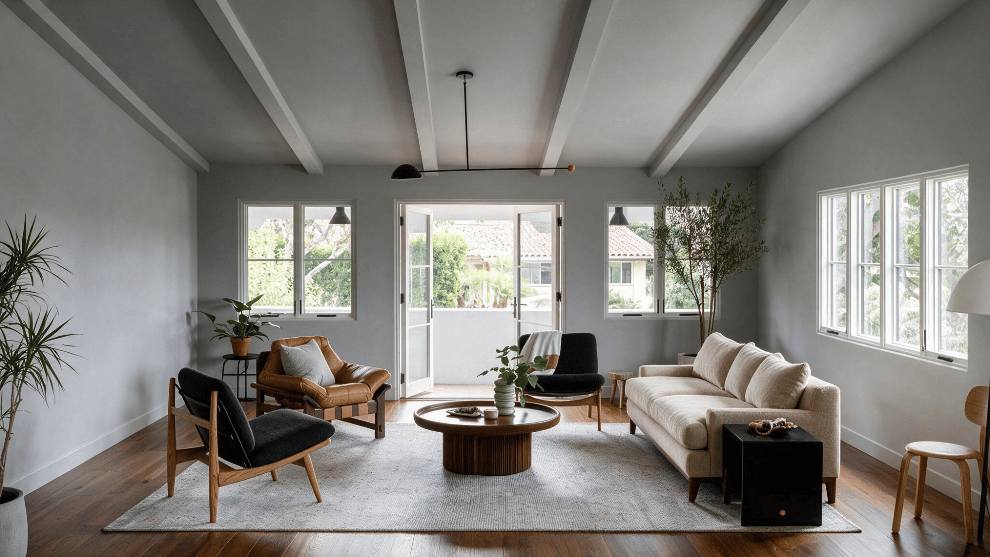 spacious modern living room with white sofa wooden chairs round coffee table plants and large sunlit windows