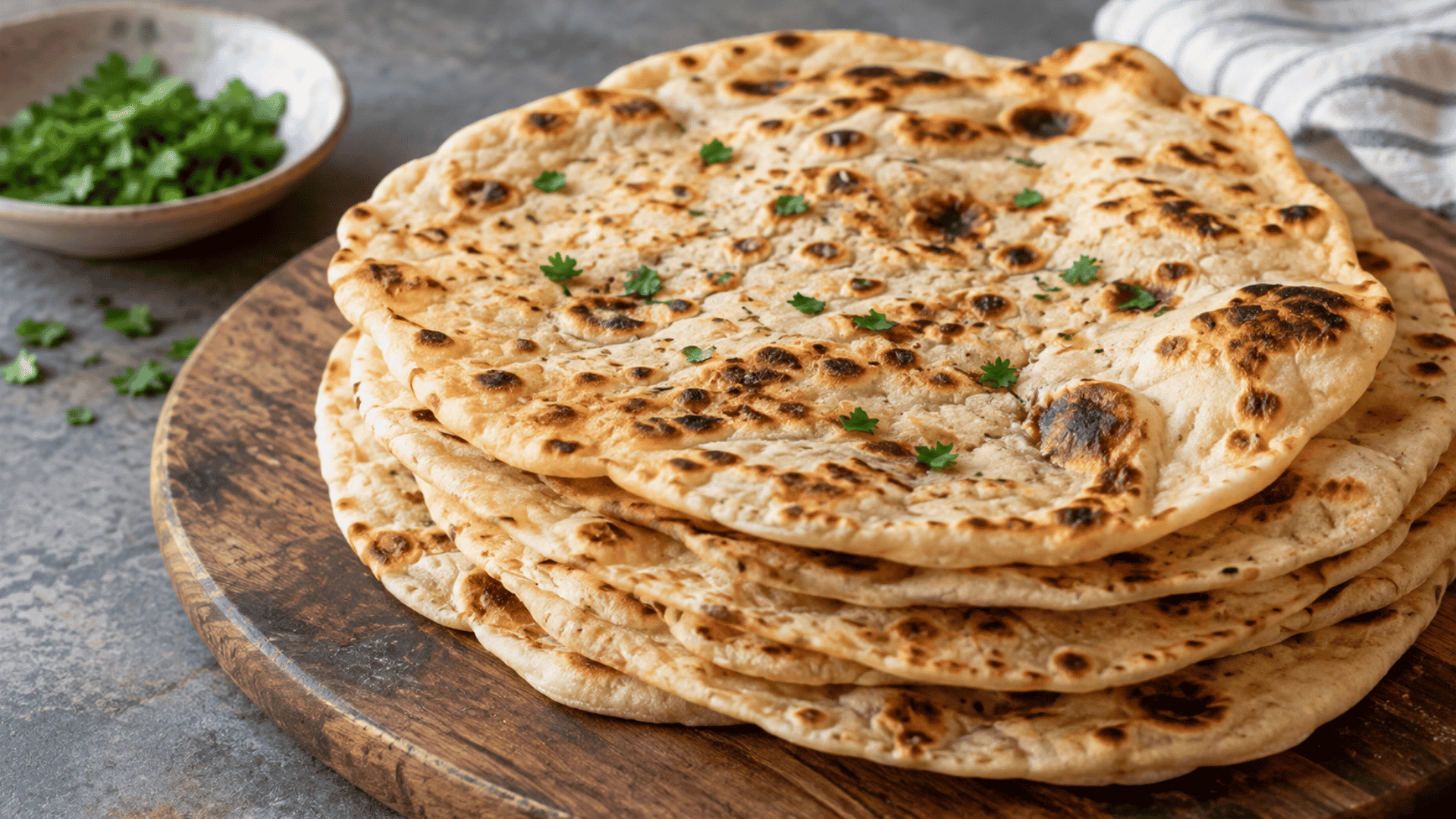 a stack of freshly cooked gluten free flatbread with golden charred spots and fresh herbs served on a wooden board