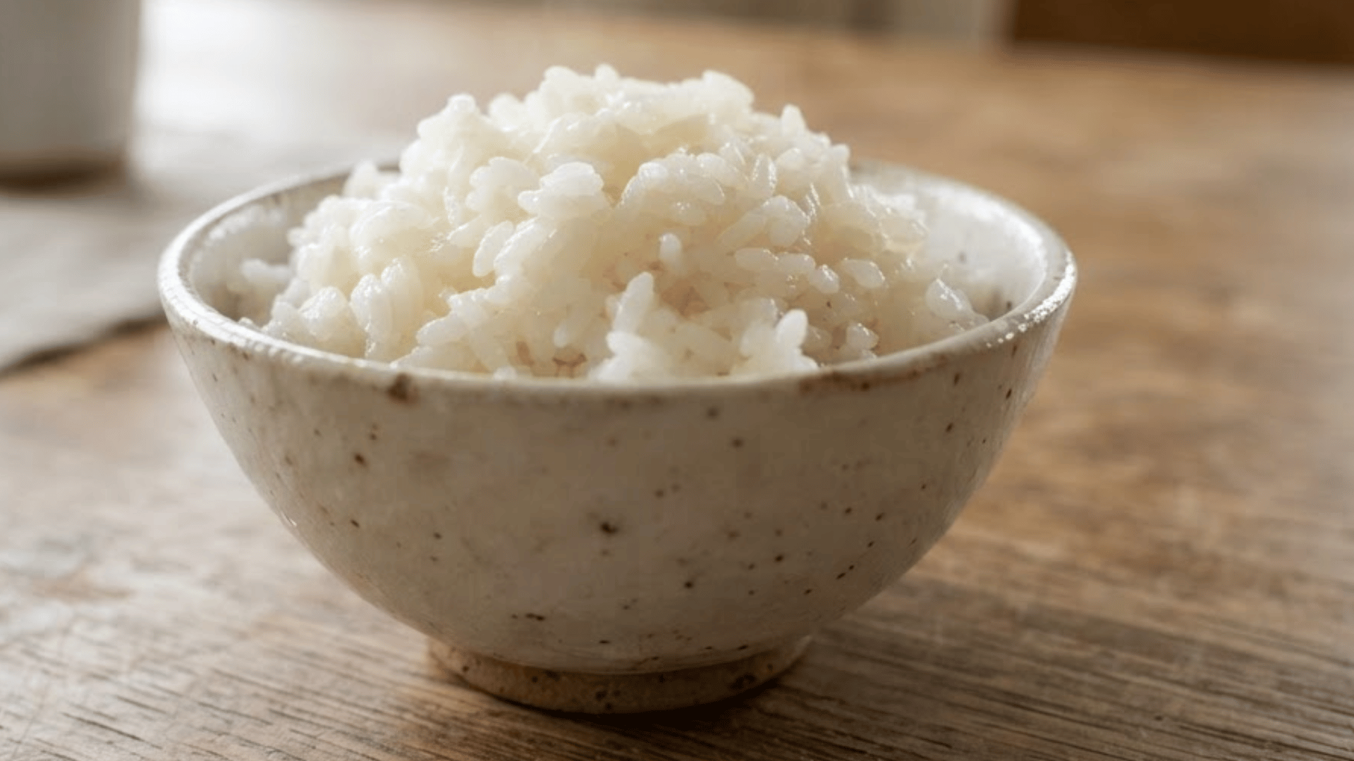 bowl of fluffy white rice served in a speckled ceramic bowl on a wooden table