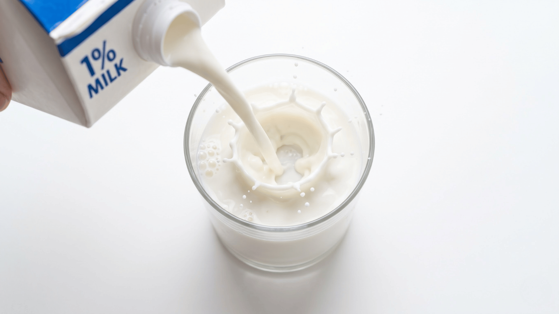 1 percent low fat milk poured into a clear glass beside a fresh carton on a clean kitchen counter