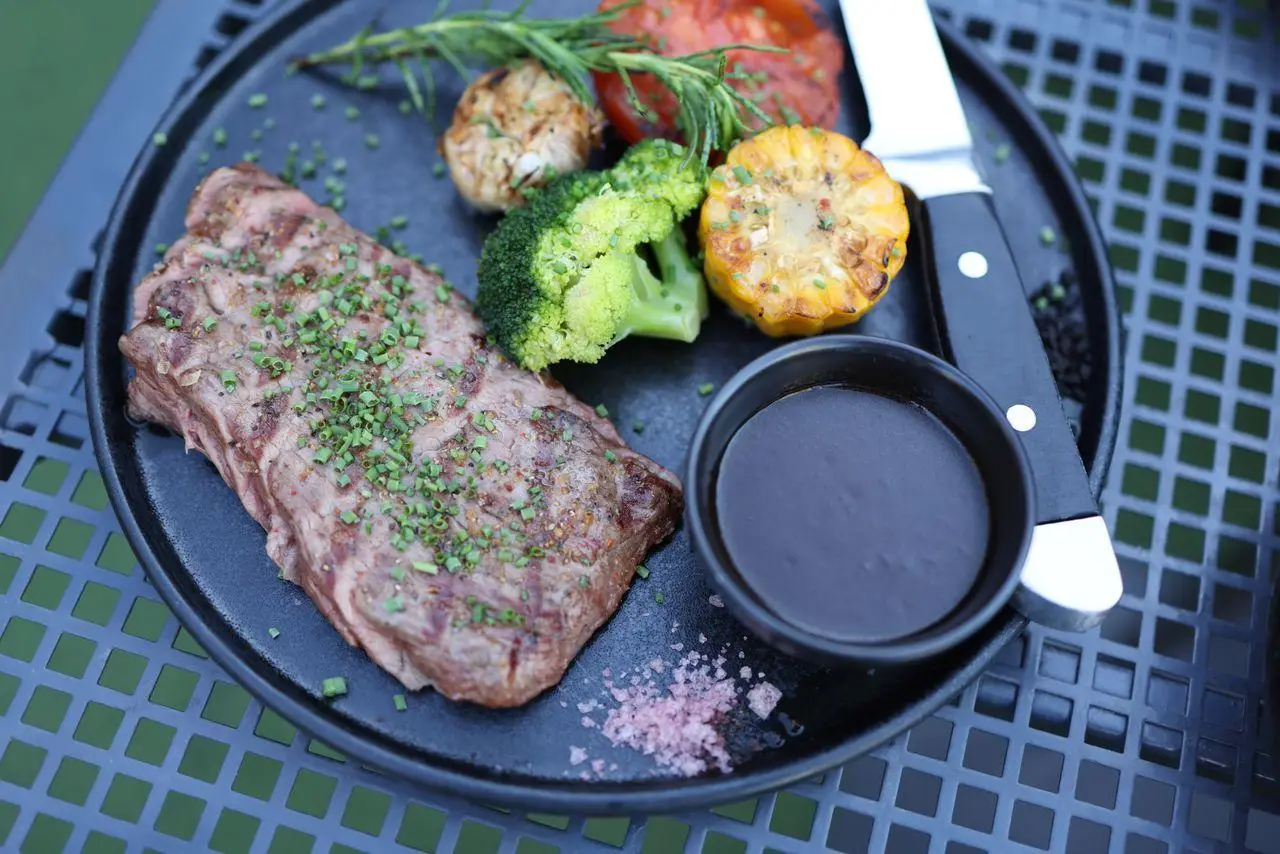 Grilled steak and vegetables on black plate with dipping sauce on outdoor metal table